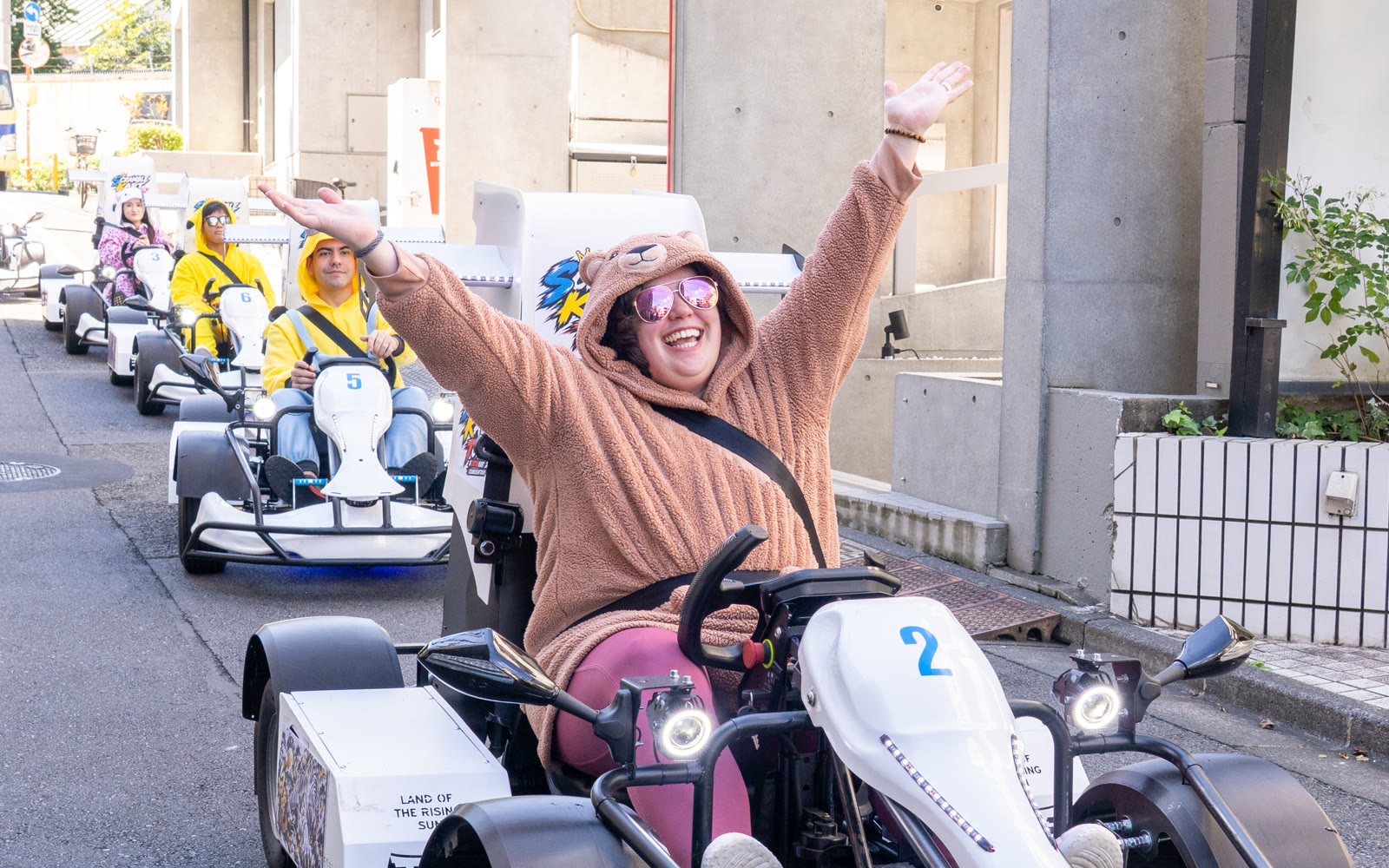 A guest in a character onesie driving a SCRAMBLE KART TOKYO go-kart on a Tokyo street
